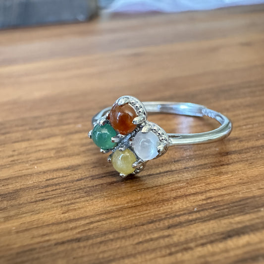 Multicolored gemstone flower ring with crystal accents on a vintage silver band, displayed on a textured wood background.
