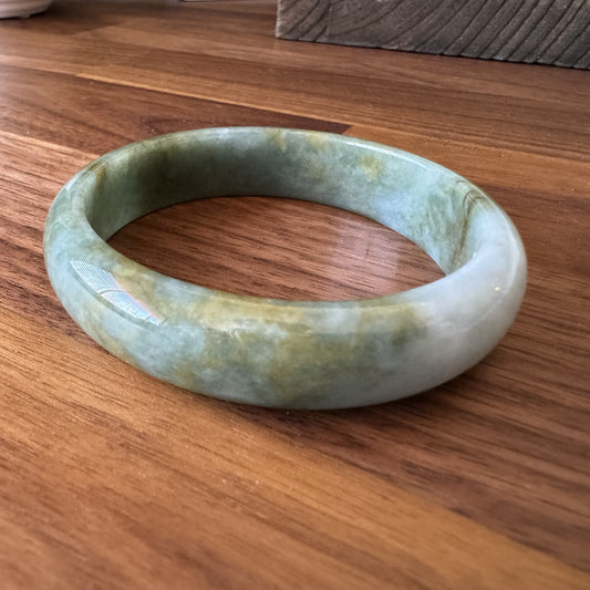 Polished green jade bangle with marbled texture on a wooden background, ideal for traditional and modern fashion styles.