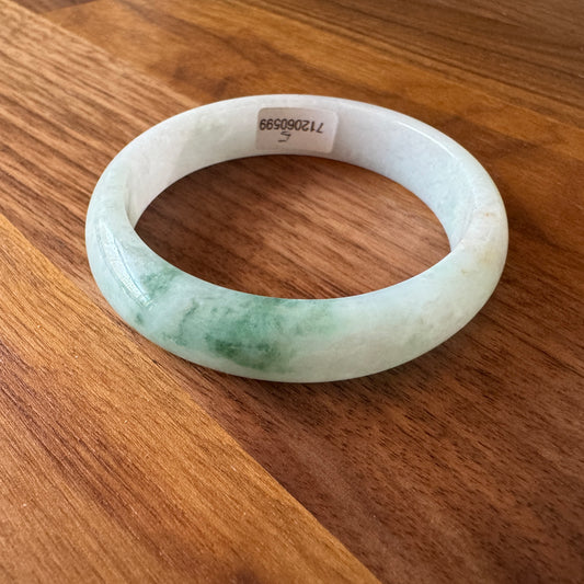 Polished Grade-A jadeite bangle with unique green accents on a wooden surface, showcasing natural elegance and luxury.