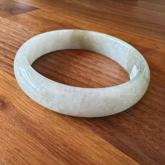 Translucent jadeite bangle with natural green and white variations on a wooden background.